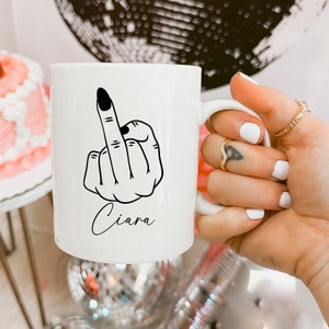 Peut inclure: Une tasse en céramique blanche avec un dessin de majeur noir et le nom "Ciara" imprimé au bas.