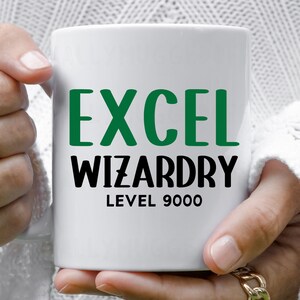 Op de afbeelding: Een witte keramische mok met de tekst EXCEL in het groen, gevolgd door WIZARDRY in het zwart, en LEVEL 9000 in het zwart eronder. De mok heeft een glad, cilindrisch lichaam en een handvat aan de zijkant met duidelijke, dikke letters op de voorzijde.