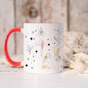 May include: White ceramic mug with a red handle and interior. The mug features line art illustrations of yoga poses, with accents of pink and yellow. Black star and leaf designs are scattered around the yoga figures.
