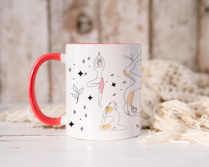 May include: White ceramic mug with a red handle and interior. The mug features line art illustrations of yoga poses, with accents of pink and yellow. Black star and leaf designs are scattered around the yoga figures.