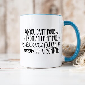 May include: White ceramic mug with a blue handle and rim. The mug features black text that reads "YOU CAN'T POUR FROM AN EMPTY MUG. HOWEVER YOU CAN THROW IT AT SOMEONE."