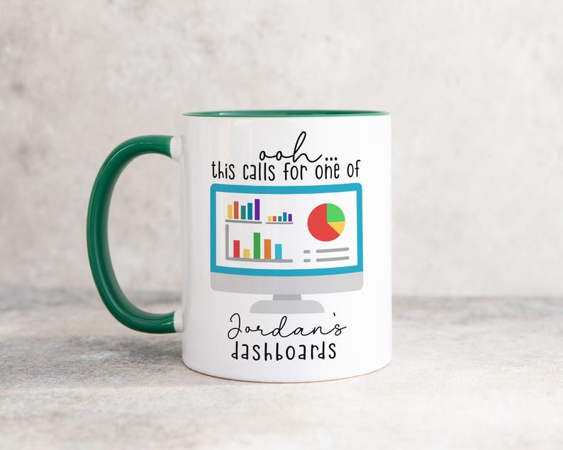 May include: A white ceramic mug with a dark green handle and interior. The front features a graphic of a computer monitor displaying colorful bar and pie charts, with the text "ooh... this calls for one of Jordan's dashboards" in black script.