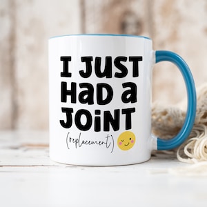 May include: A white ceramic mug with a blue interior and handle. The front features bold black text that reads I JUST HAD A JOINT (replacement) followed by a small yellow winking smiley face icon with pink cheeks on the lower right side.