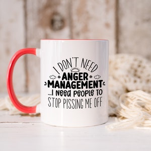 Może przedstawiać: Biały kubek ceramiczny z czerwonym rantem i uchwytem. Kubek ma czarny napis: "I don't need #ANGER* -MANAGEMENT... I need people to STOP PISSING ME OFF".