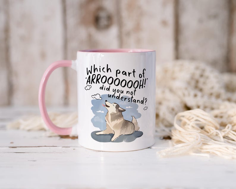 May include: A white ceramic mug with a pink handle and interior rim. The mug features a graphic of a howling dog and the text: Which part of ARROOOOOOH! did you not understand? The dog is light brown and white, positioned against a blue sky.