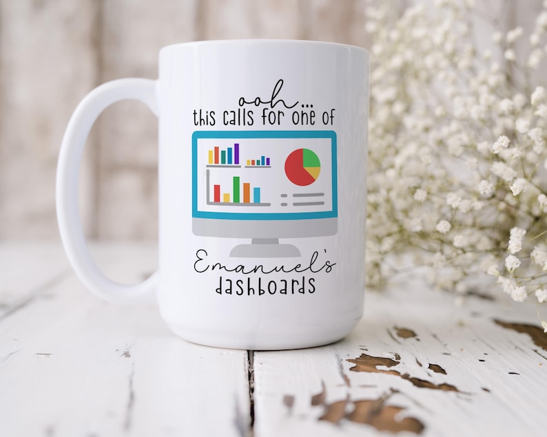 May include: A white ceramic mug featuring a graphic of a computer monitor displaying colorful bar and pie charts. The text above the monitor reads "ooh... this calls for one of" and the text below reads "Emanuel's dashboards" in black script and print.
