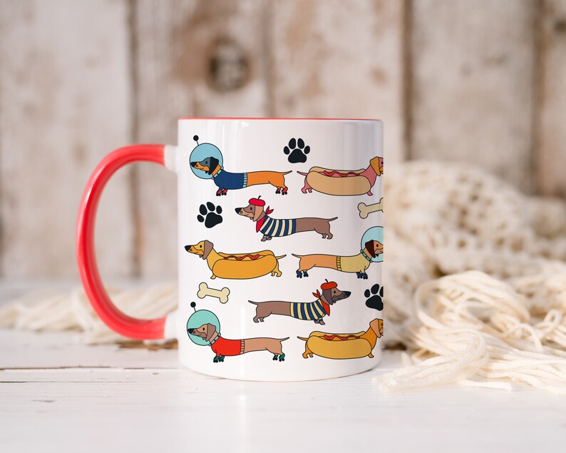May include: White ceramic coffee mug with a red rim and handle. The mug features a repeating pattern of cartoon dachshunds wearing different costumes, including a hot dog, a sailor, and an astronaut.