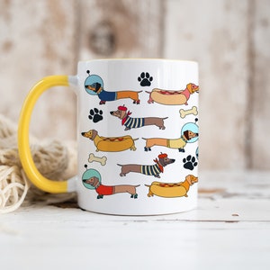 May include: White ceramic mug with a yellow handle. The mug features a repeating pattern of cartoon dachshunds wearing different outfits and accessories, including a hot dog costume, a beret, and a space helmet.