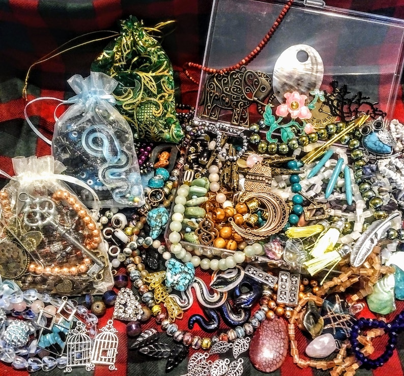 May include: A collection of colorful jewelry and trinkets, including beads, charms, and pendants. The items are arranged on a red and black plaid fabric background. Some of the items are in a clear plastic box.