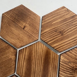 May include: Set of six hexagonal wooden coasters in a dark brown wood stain. The coasters are arranged in a honeycomb pattern.