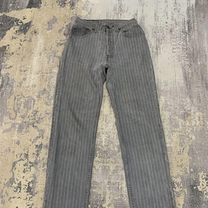 May include: Gray pinstripe jeans with a classic five-pocket design. The pants have a straight leg cut and a button and zipper closure. The fabric has vertical stripes, creating a textured appearance. The jeans are laid flat on a patterned surface.