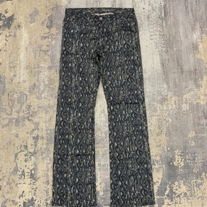 May include: Flared trousers featuring a detailed pattern in grey and white. The trousers are made of a light material and have a button and zip fastening. The garment is displayed flat on a neutral surface.