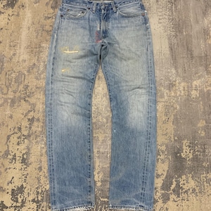 Könnte beinhalten: Hellblaue Jeans aus Denim mit verwaschenen Details und Used-Look. Die Jeans haben ein klassisches Fünf-Taschen-Design und eine gerade Beinpassform. Es gibt sichtbare Gebrauchsspuren, einschließlich verblasster Bereiche und kleiner Reparaturen.