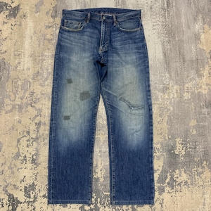 May include: Blue denim jeans with a button fly and five-pocket design. The jeans have a faded appearance with distressed patches on the legs, giving them a vintage look. The denim has a medium wash with lighter areas.