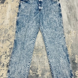 May include: Acid wash denim jeans with a classic five-pocket design. The jeans have a light blue and white speckled pattern, a button and zipper closure, and a straight leg fit. The jeans are laid flat on a textured surface.