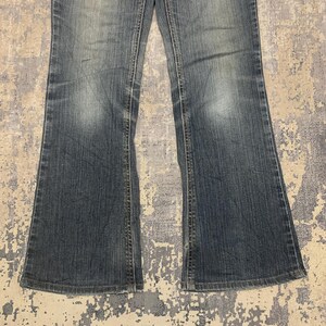 Op de afbeelding: Verbleekte blauwe denim jeans met een uitlopend pijp ontwerp. De jeans hebben een klassieke vijf-zakken stijl en een knoop- en ritssluiting. De denim heeft een versleten uiterlijk met subtiele vervaging en kreukels.