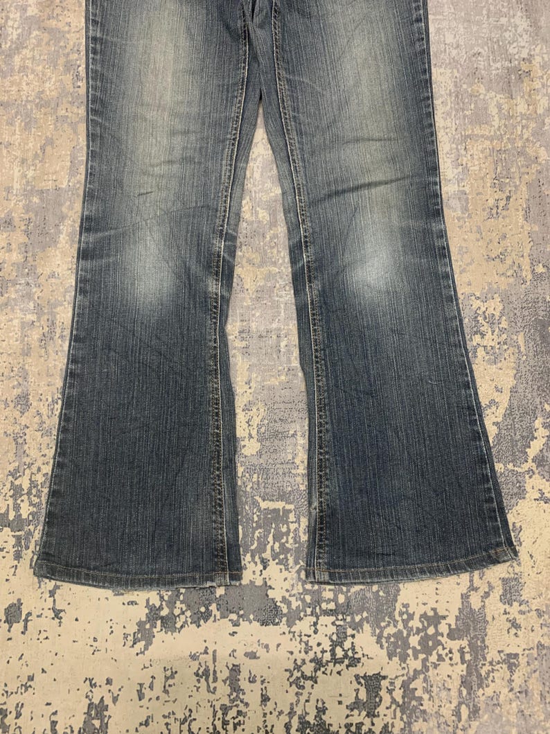Op de afbeelding: Verbleekte blauwe denim jeans met een uitlopend pijp ontwerp. De jeans hebben een klassieke vijf-zakken stijl en een knoop- en ritssluiting. De denim heeft een versleten uiterlijk met subtiele vervaging en kreukels.