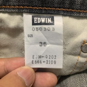 Pode incluir: Close-up de uma etiqueta de jeans Edwin. A etiqueta branca apresenta texto preto, incluindo a marca, c&oacute;digos de produto e tamanho 36. Os jeans s&atilde;o de cor cinza escuro.