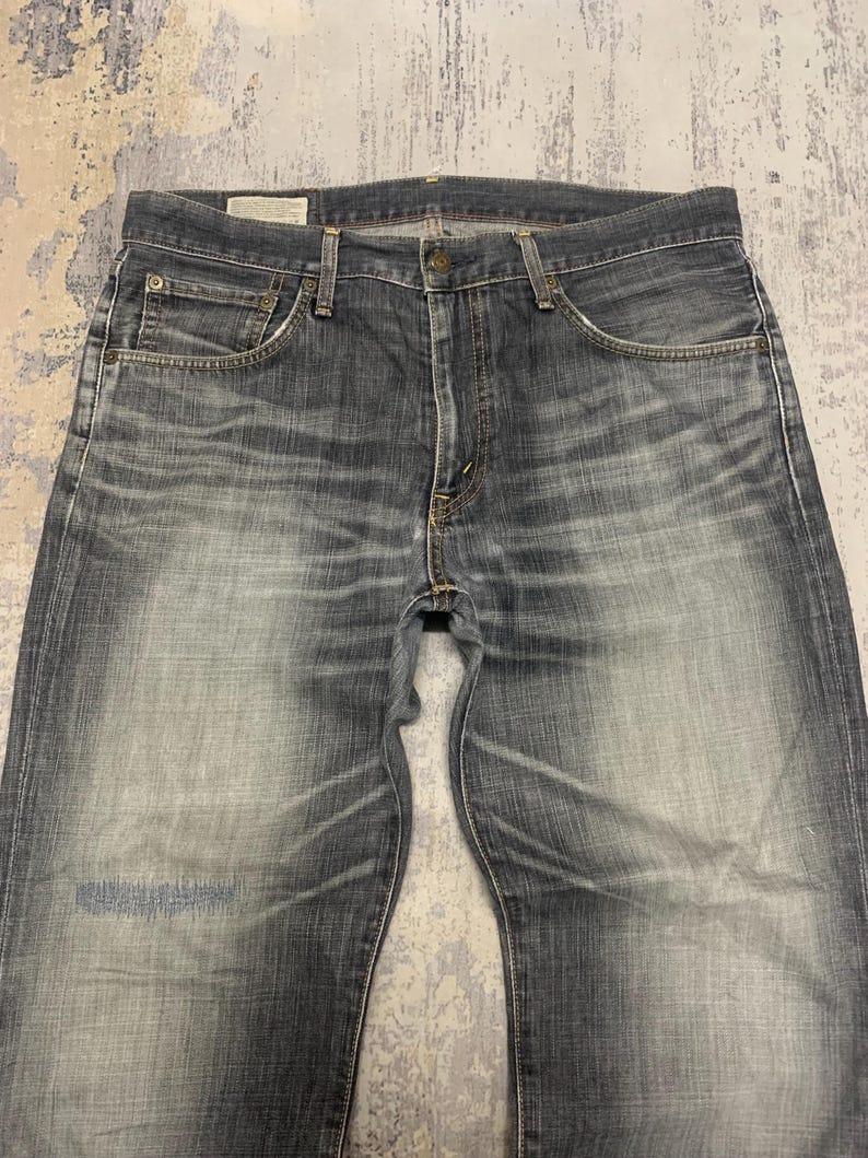 Pode incluir: Jeans de ganga azul desbotada com um design cl&aacute;ssico de cinco bolsos. Os jeans t&ecirc;m fecho de bot&atilde;o e z&iacute;per, presilhas para cinto e uma lavagem clara com desbotamento sutil e marcas de desgaste.