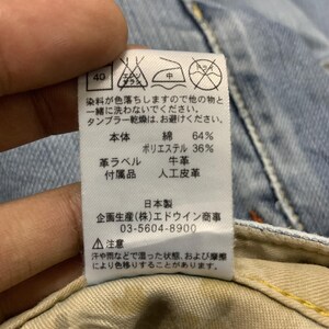 Puede incluir: Primer plano de una etiqueta con texto japon&eacute;s y s&iacute;mbolos de cuidado. La etiqueta indica que la composici&oacute;n del tejido es 64% algod&oacute;n y 36% poli&eacute;ster. Tambi&eacute;n menciona que el producto est&aacute; fabricado en Jap&oacute;n y proporciona un n&uacute;mero de tel&eacute;fono.
