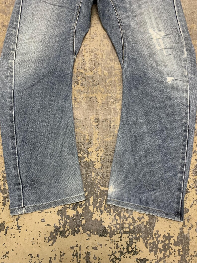 Puede incluir: Vaqueros de mezclilla azul claro con detalles desgastados. Los vaqueros tienen un dise&ntilde;o cl&aacute;sico de cinco bolsillos, una bragueta con cremallera y un corte recto. La mezclilla tiene un lavado descolorido y sutiles bigotes.