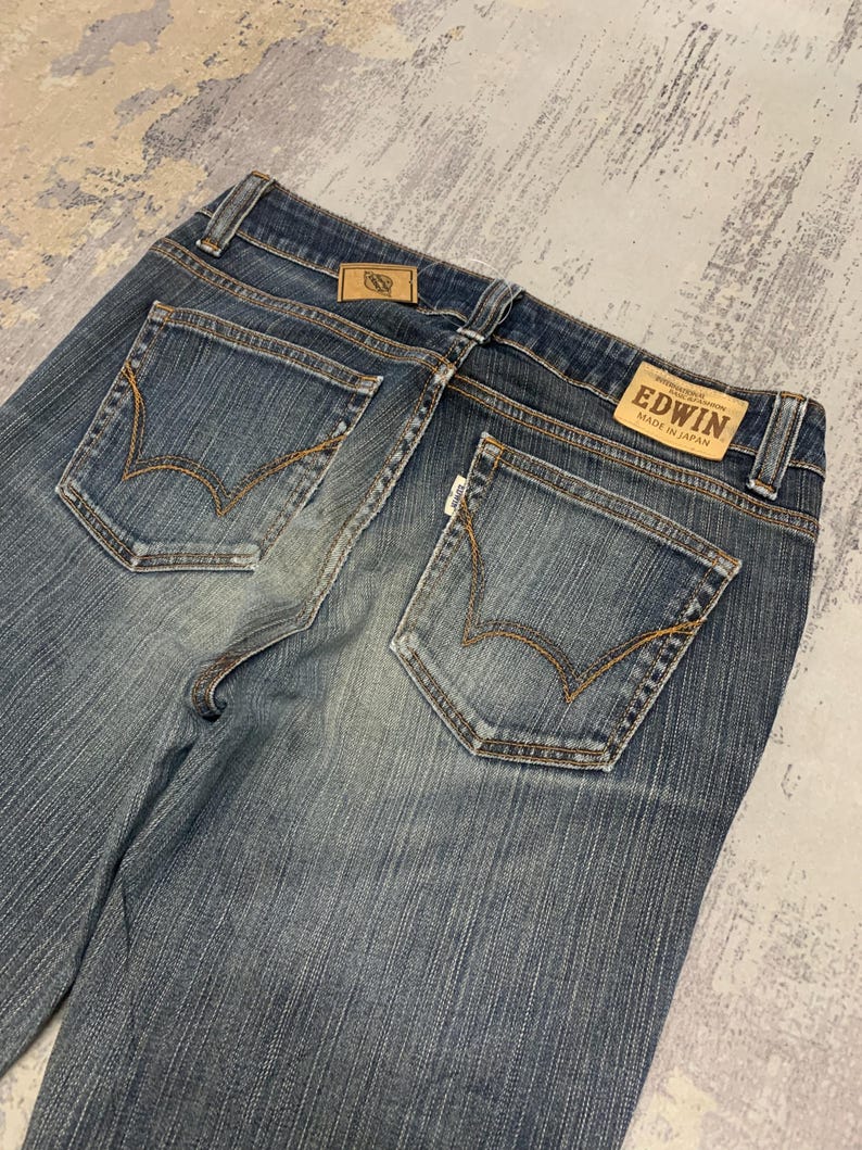 Op de afbeelding: Blauwe jeans met een vervaagde wassing. De jeans heeft twee achterzakken met decoratieve stiksels en een leren label met de merknaam "EDWIN MADE IN JAPAN".