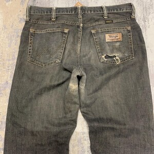 Pu&ograve; includere: Jeans Wrangler neri sbiaditi con un aspetto usurato. I jeans hanno un classico stile a cinque tasche, una toppa in pelle e il logo Wrangler. La tasca posteriore presenta una cucitura a "W" distintiva.