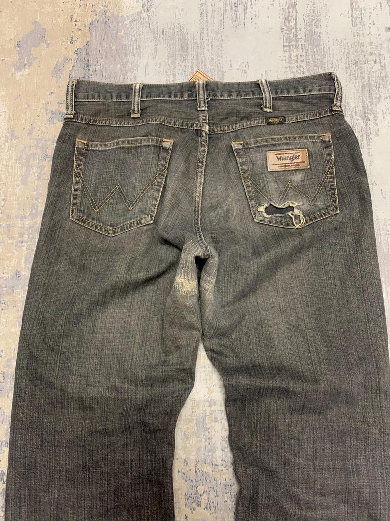 Pu&ograve; includere: Jeans Wrangler neri sbiaditi con un aspetto usurato. I jeans hanno un classico stile a cinque tasche, una toppa in pelle e il logo Wrangler. La tasca posteriore presenta una cucitura a "W" distintiva.