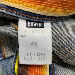 Może przedstawiać: Zbliżenie na element odzieży dżinsowej z metką marki EDWIN. Na metce widnieje rozmiar 44 oraz inne kody produktu. Wewnętrzna podszewka ma kolorowy wz&oacute;r w paski w odcieniach pomarańczu, ż&oacute;łci i brązu.