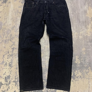 Könnte beinhalten: Dunkelblaue Jeans. Die Jeans haben ein klassisches Fünf-Taschen-Design mit Knopfleiste. Der Denim scheint ein mittleres Gewicht zu haben, mit einigen Ausbleichungen und Gebrauchsspuren. Die Jeans liegen flach auf einer gemusterten Oberfläche.
