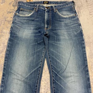 May include: Blue denim jeans with a classic five-pocket design. The jeans have a faded wash and a straight leg cut. Features include a button and zipper closure, and belt loops. The jeans are made of durable denim material.