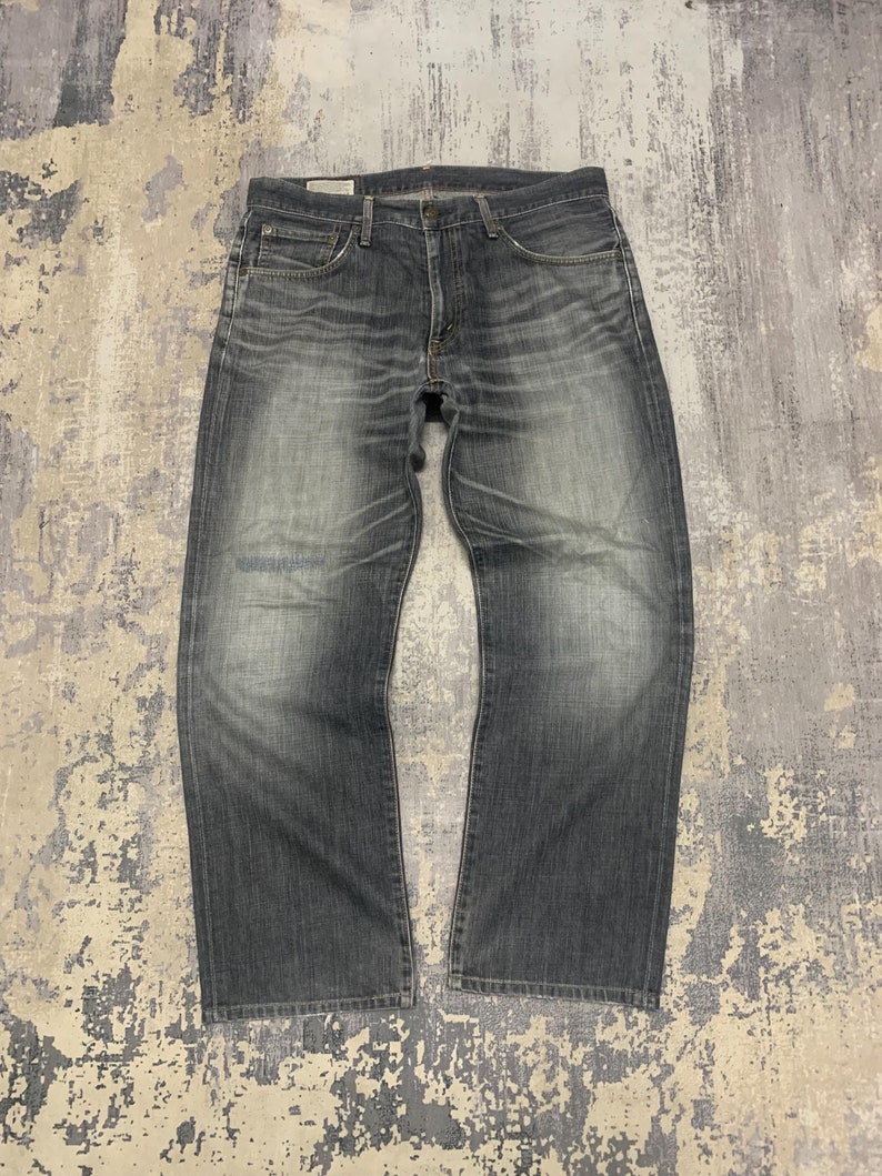 May include: A pair of faded gray denim jeans. The jeans have a classic five-pocket design, a button and zipper closure, and a straight leg cut. The denim has a worn appearance with lighter areas on the thighs and knees.