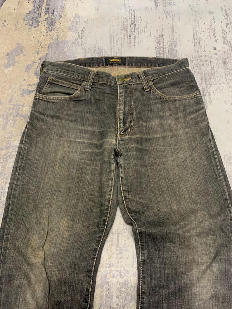 Pu&ograve; includere: Un paio di jeans Wrangler neri sbiaditi. I jeans hanno un classico design a cinque tasche, una chiusura con bottone e cerniera e un'etichetta Wrangler in vita. Il denim ha un aspetto usurato e vissuto con cuciture visibili.
