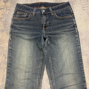 Op de afbeelding: Verbleekte blauwe denim jeans met een klassiek ontwerp met vijf zakken. De jeans hebben een knoop- en ritssluiting, riemlussen en een licht versleten uiterlijk. De denim is een medium wassing met subtiele vervaging.