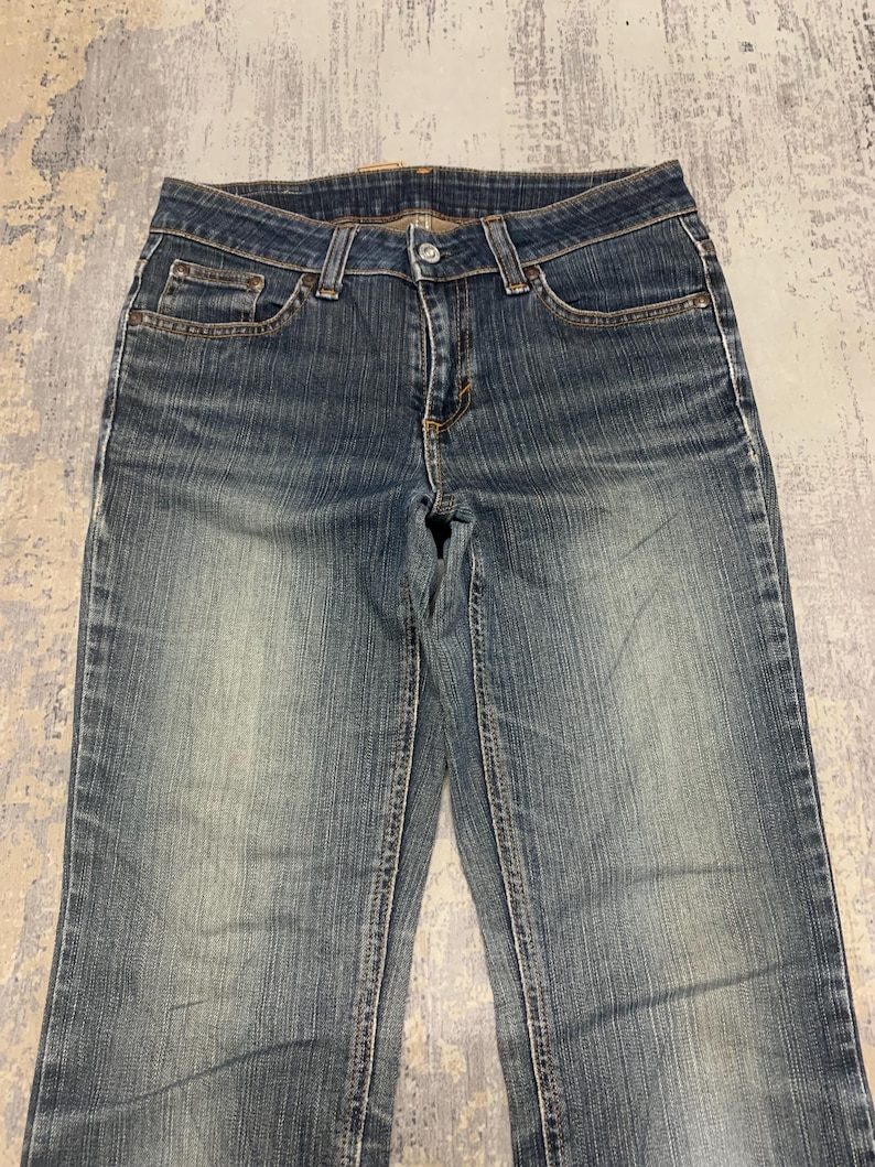 Op de afbeelding: Verbleekte blauwe denim jeans met een klassiek ontwerp met vijf zakken. De jeans hebben een knoop- en ritssluiting, riemlussen en een licht versleten uiterlijk. De denim is een medium wassing met subtiele vervaging.
