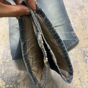 Op de afbeelding: Close-up van lichtblauwe denim jeans. De jeans is opgevouwen en onthult de binnenvoering en naden. De denim heeft een vervaagde uitstraling, met zichtbare slijtage. De stof is van een gemiddeld gewicht, geschikt voor dagelijks gebruik.