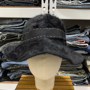 May include: A black, fuzzy hat with a wide brim and a black ribbon band. The band is accented with white stitching. The hat is displayed on a mannequin head.