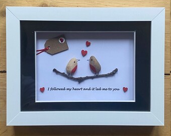 May include: Framed pebble art featuring two birds perched on a branch with red hearts surrounding them. The text "I followed my heart and it led me to you" is written below the birds.