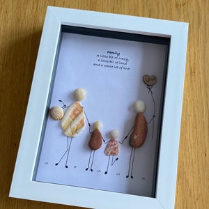 Può includere: Un'opera d'arte incorniciata che rappresenta una famiglia di quattro persone realizzata con piccole pietre e conchiglie. L'opera include il testo "Family, A little bit of crazy, a little bit of loud and a whole lot of love." e una pietra a forma di cuore con la parola "Love" su di essa.