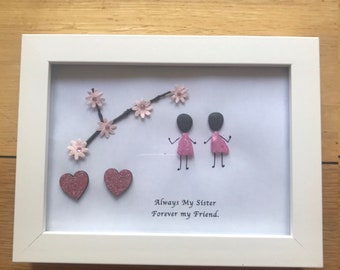 May include: A framed artwork featuring two figures in pink dresses and two glittery hearts. A branch with pink flowers and the text "Always My Sister Forever my Friend" are also included.
