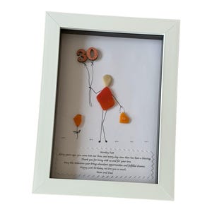 May include: A white framed picture with a hand-drawn figure made of colorful stones holding a balloon with the number 30 on it. The picture includes a message that reads "Thirty years ago you came into our love, and every day since then has been a blessing. Thank you for being with us and for your love. May this milestone bring abundance, opportunities and fulfilled dreams. Happy 30th Birthday, we love you so much. Mom and Dad."