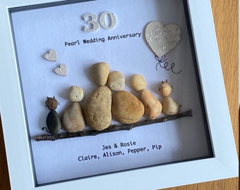 May include: A framed pebble art piece celebrating a 30th wedding anniversary. The art features a family of five, two cats, and a heart-shaped balloon with the text "tee". The text "30 Pearl Wedding Anniversary" is at the top of the frame. The names "Jes & Rosie, Claire, Alison, Pepper, Pip" are at the bottom of the frame.