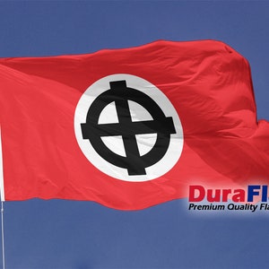 Op de afbeelding: Een rode vlag met een witte cirkel en een zwart Keltisch kruisontwerp, wapperend in de wind tegen een blauwe lucht. De vlag is bevestigd aan een witte vlaggenmast. De tekst "DuraFlag Premium Quality Flags" is zichtbaar.