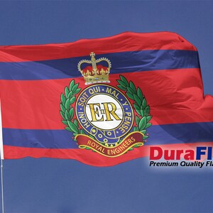 May include: A red and blue flag with the Royal Engineers emblem, featuring a crown, laurel wreath, and the text "Royal Engineers." The flag is on a white pole against a blue sky. The text "DuraFlag" is visible.