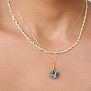 Puede incluir: Un collar de cadena de cuerda dorada con un colgante de piedra preciosa verde y negra.