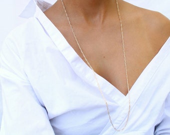 May include: A gold chain necklace worn by a person wearing a white shirt.