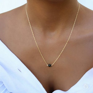 Pu&ograve; includere: Una delicata collana a catena dorata con un ciondolo a forma di perla nera.
