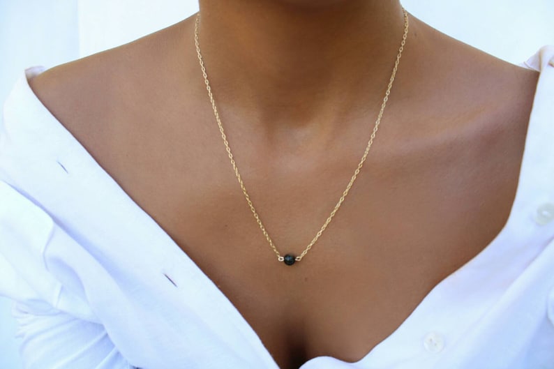 Pu&ograve; includere: Una delicata collana a catena dorata con un ciondolo a forma di perla nera.