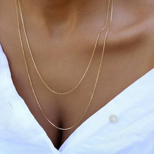 May include: Three gold chain necklaces layered on a person's neck. The chains are thin and delicate.