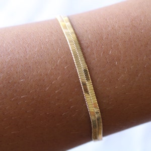 Puede incluir: Un brazalete de cadena dorada con un diseño de cadena de serpiente.